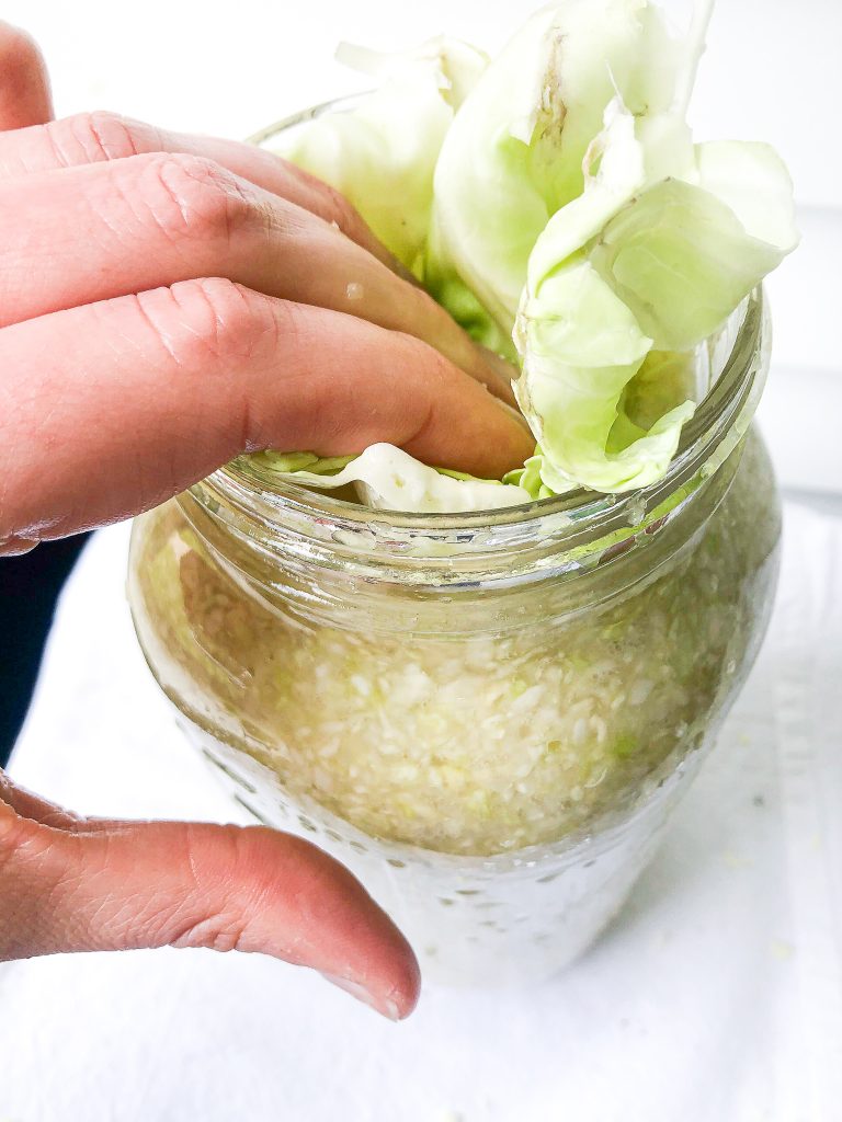 hand pushing cabbage leaves into a jar of sauerkraut