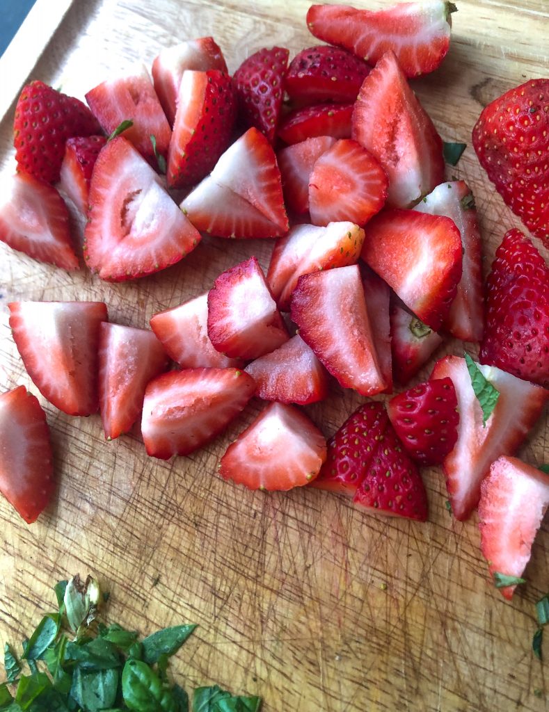 close up shot of strawberries cut up on a cutting board.