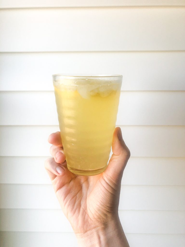 glass of naturally sweetened honey lemonade held by hand against white wall