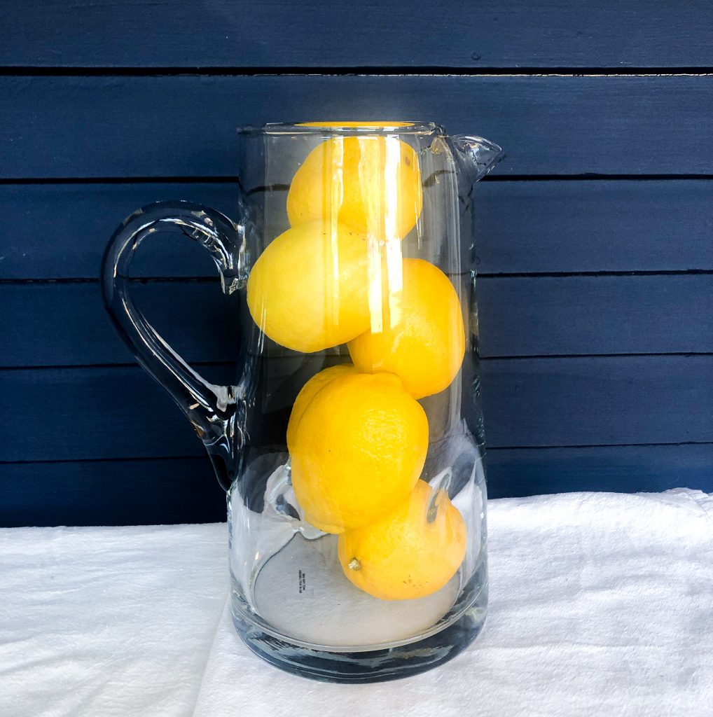 lemons in a glass pitcher against a navy blue wall