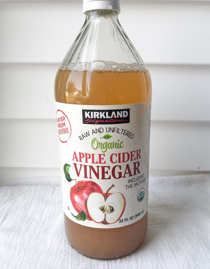large jar of apple cider vinegar on against a white wall.