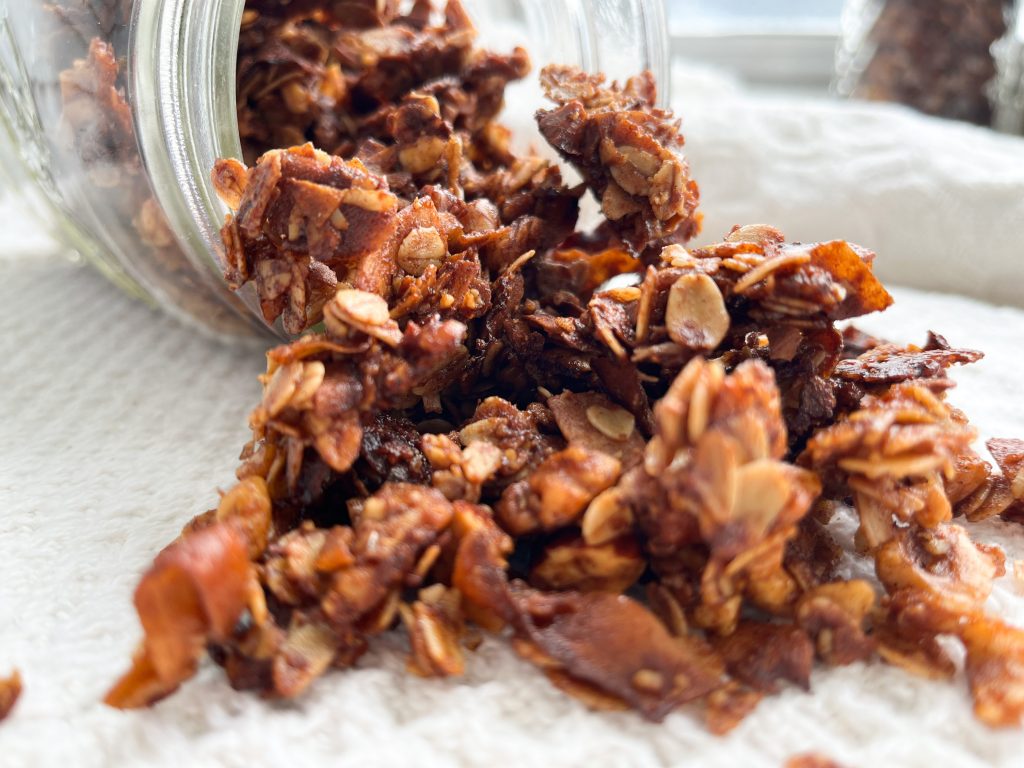 crunchy granola spilling out of a jar laying on table