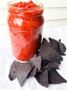 red salsa in a jar next to blue corn chips