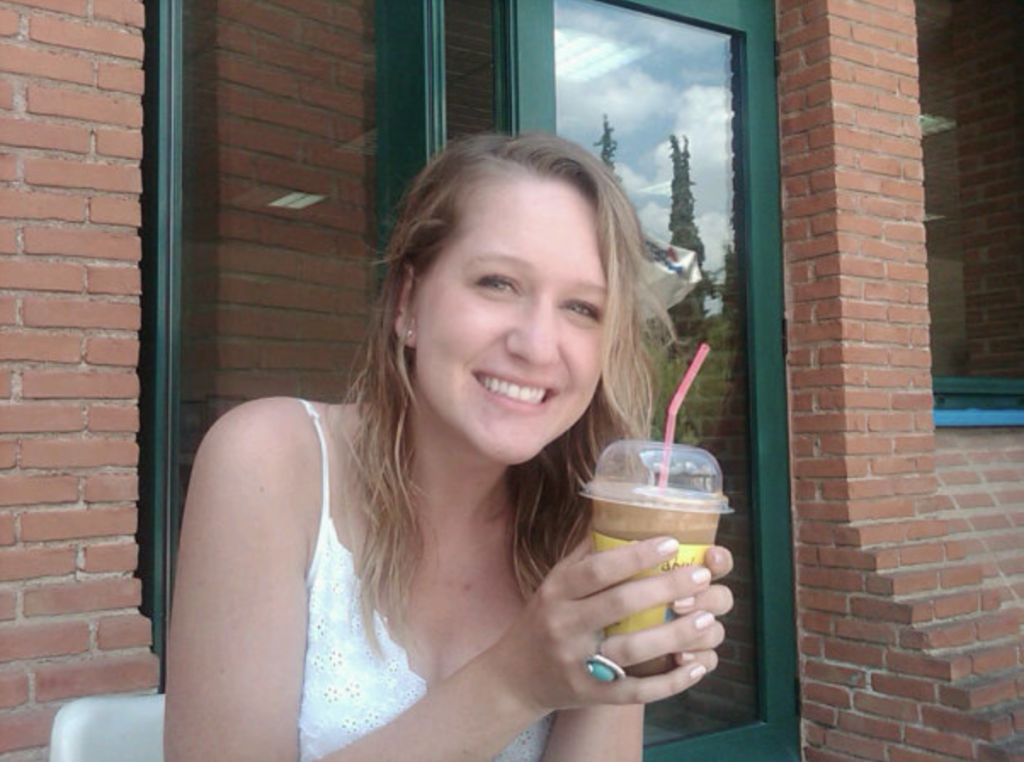 woman in white dress sitting outside holding an iced coffee drink in her hands.