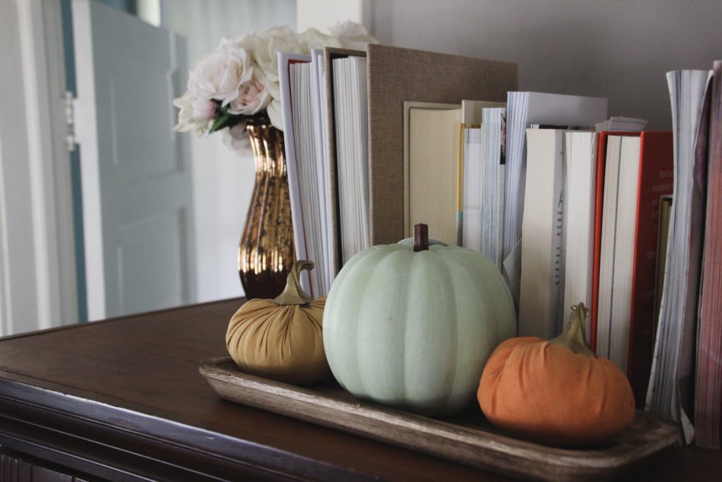 artificial colored pumpkins on a tray in front of stacked books