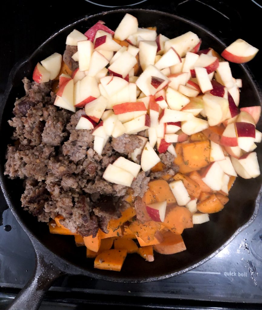 sweet potatoes, apple and sausage in a skillet on a stove.