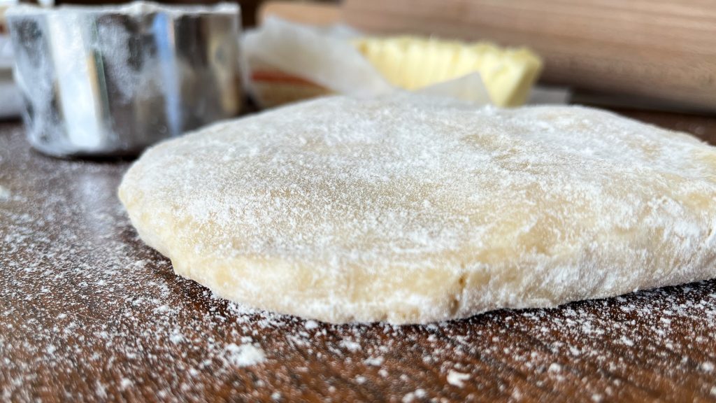 quick and easy make ahead pie crust dough on a wooden table with flour sprinkled around it with butter and a rolling pin in the background