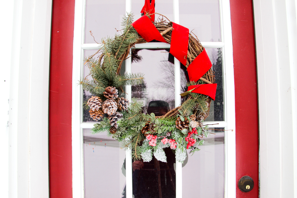 Christmas wreath hanging on door with red ribbon