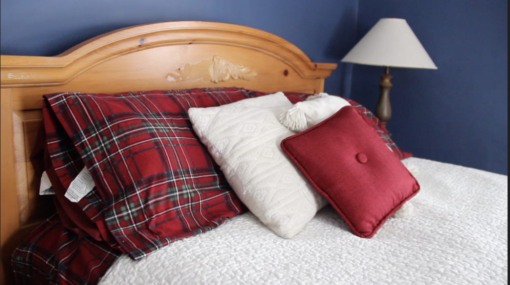 Bed mad with red and green Christmas plaid bed sheets, a white comforter and a white throw pillow
