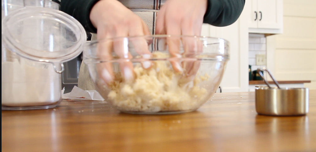 woman's hands squishing quick and easy make ahead pie crust dough in a glass bowl on a wooden counter top