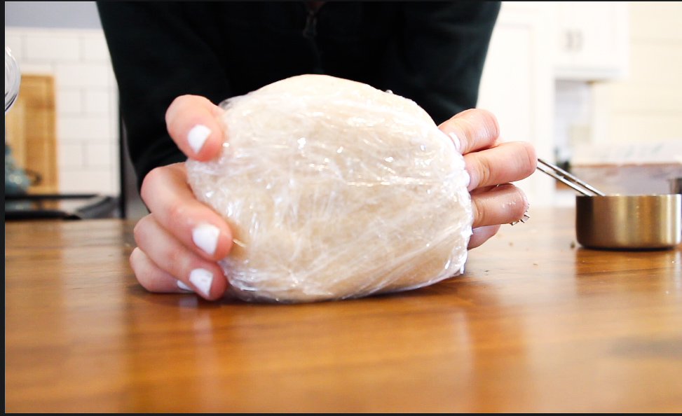 woman's hands holding a quick and easy make ahead pie crust on a wooden counter top