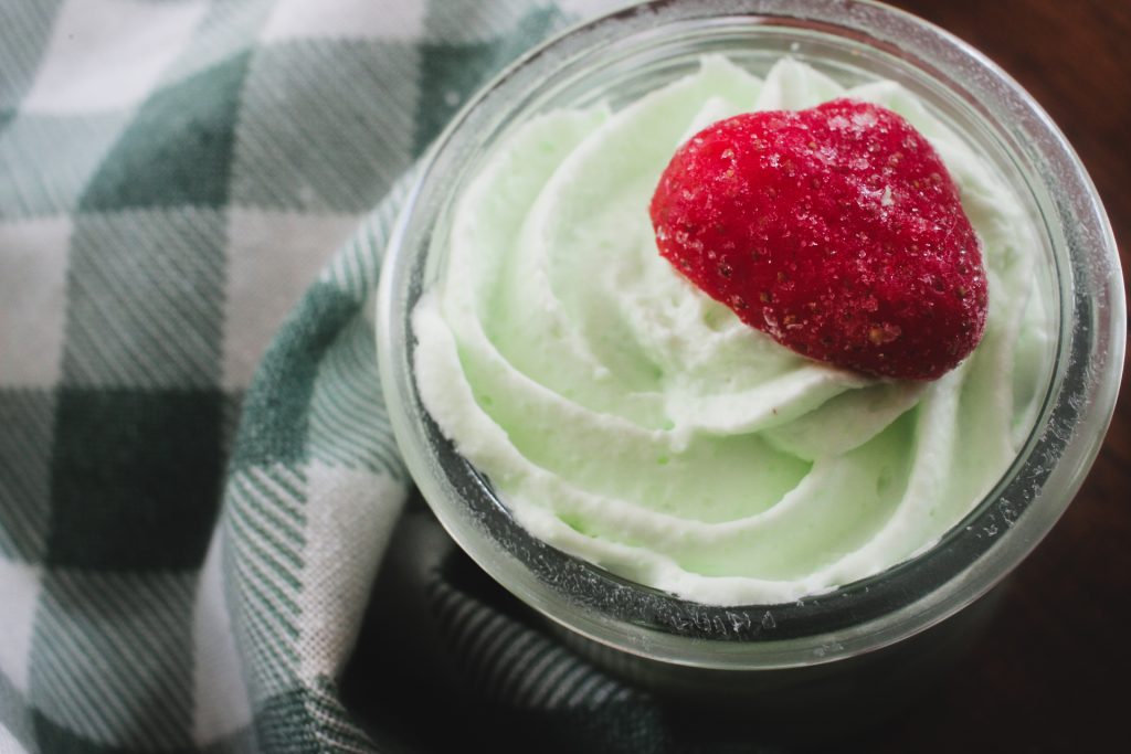mousse in a glass jar with a strawberry on top in front of a green gingham towel